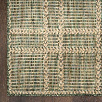 Green and beige woven area rug with geometric chevron and stripe patterns on dark wood floor.