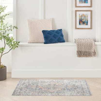 Soft pink knitted cushion & blue geometric-knit cushion on a white window-seat with beige fringe throw; plant & blue rug