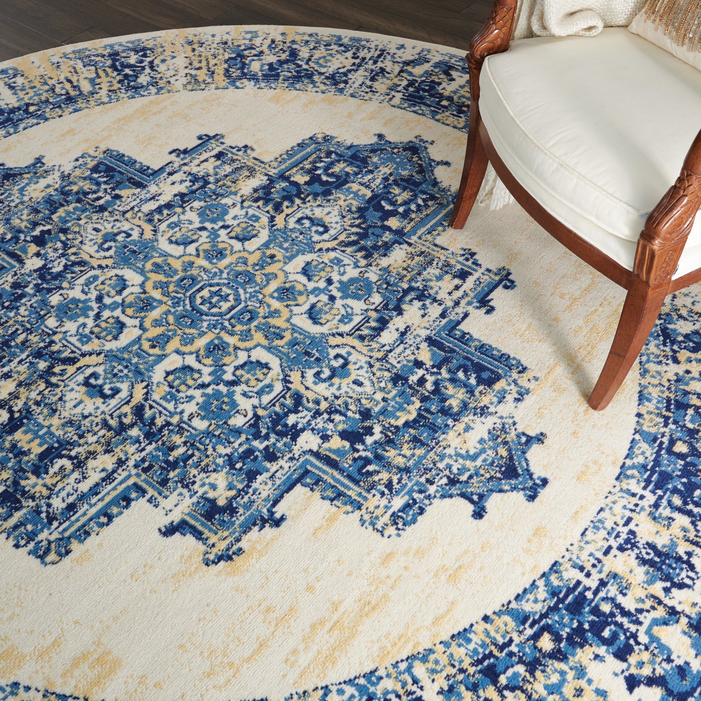 Circular blue and beige oriental rug with an intricate floral pattern; wood-framed cream-upholstered chair on the edge.