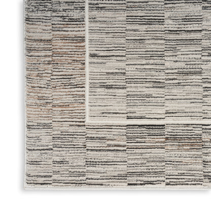 Neutral patchwork area rug with striped blocks in cream, beige, gray and black; textured tufted pile.