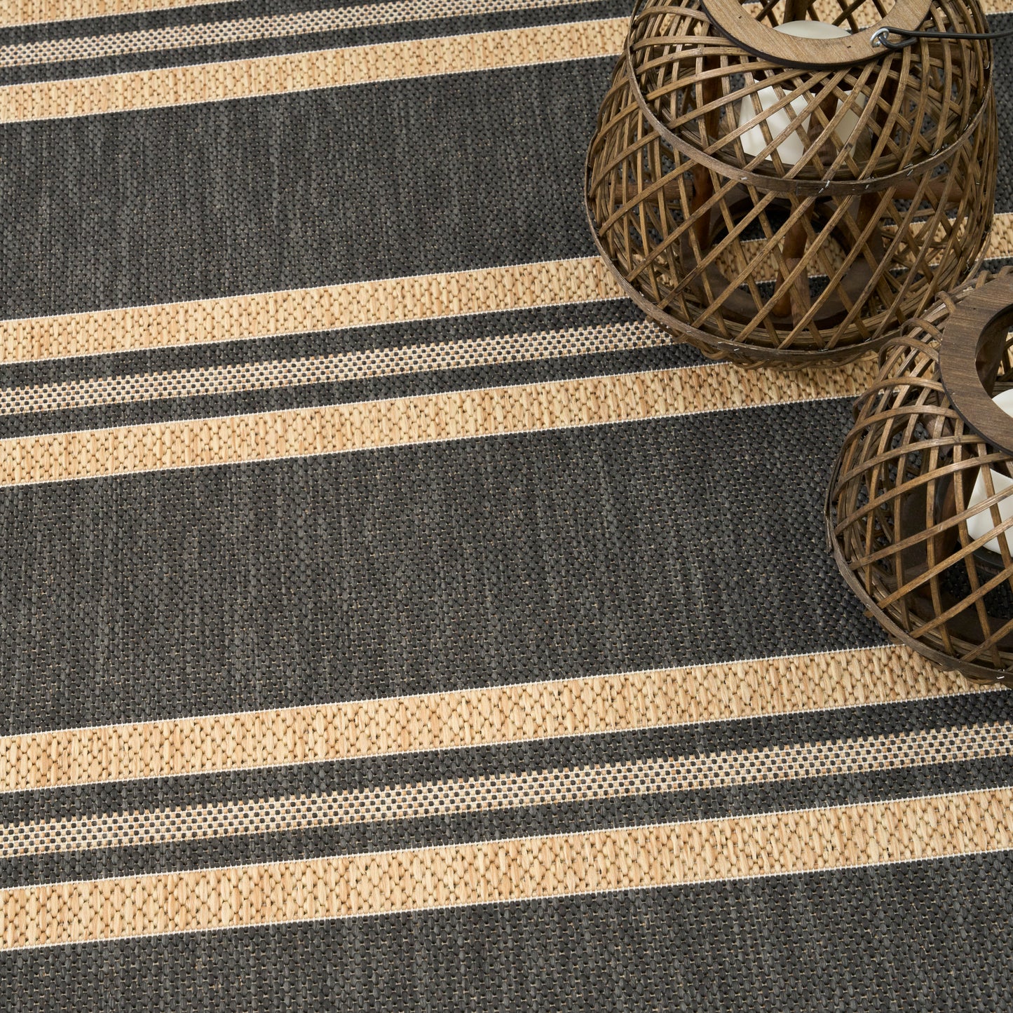 Dark gray and tan striped woven rug with textured stripes; round wicker lanterns add rustic decor.