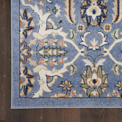 Blue oriental rug corner with ivory, orange, and green floral motifs on dark wood floor.