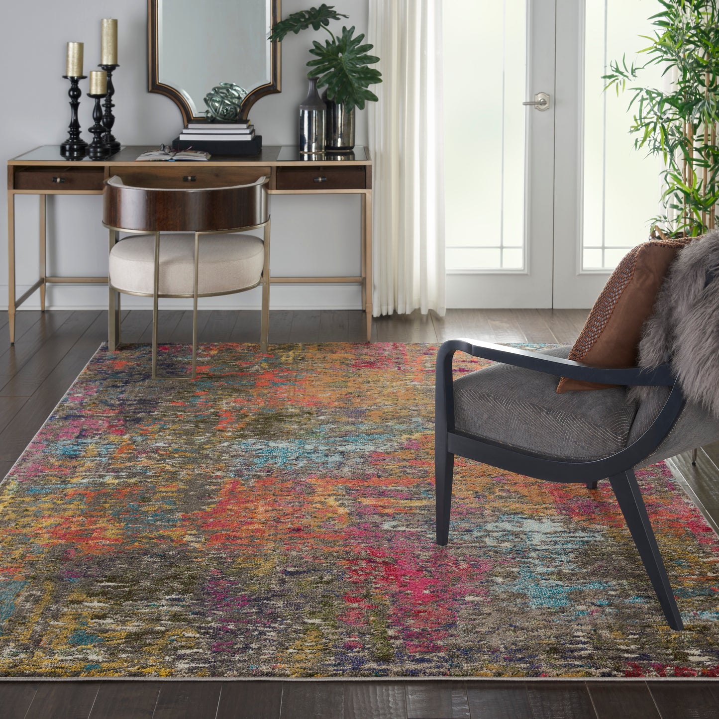 Multicolor abstract area rug on dark wood floor; contemporary living room with a wooden desk, cream upholstered chair, black-framed armchair, and plants.