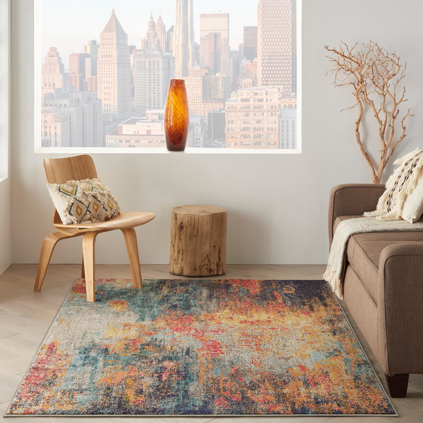 Colorful abstract area rug on light wood floor; mid-century wooden chair, amber vase, brown sofa, tree-stump side table.