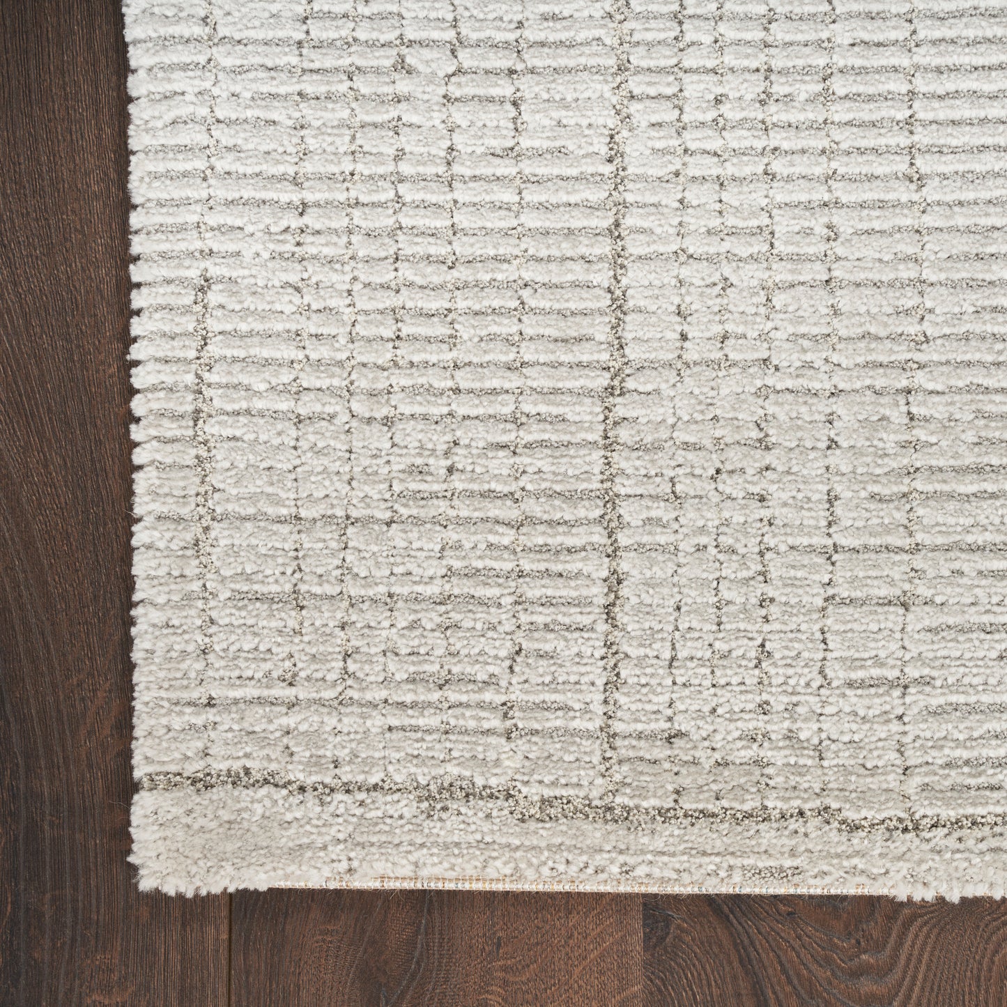 Cream textured area rug with a raised grid pattern on dark wood floor, thick edge border visible.