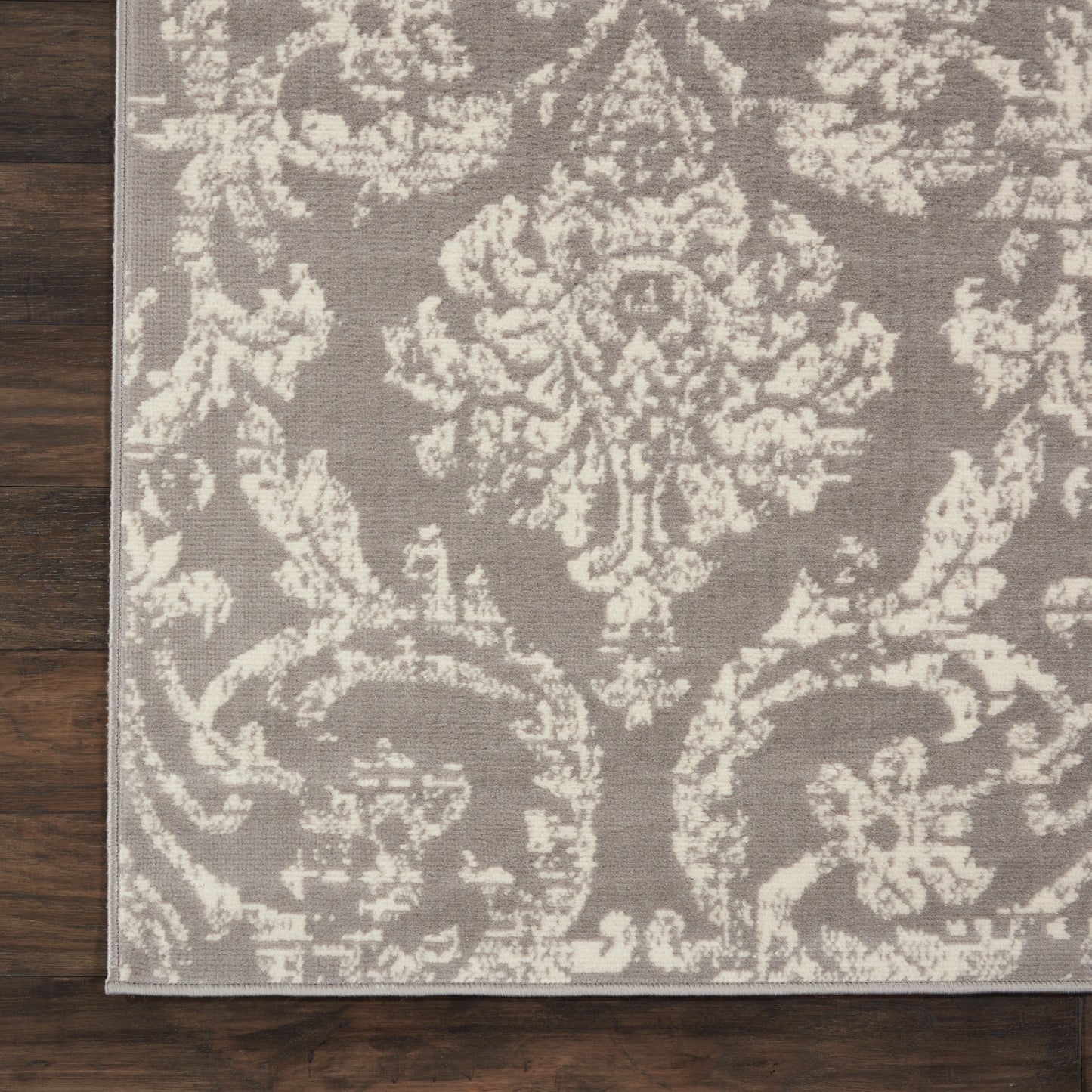 Taupe rug with ivory damask floral pattern, woven texture, rectangular with light border; placed on hardwood floor.