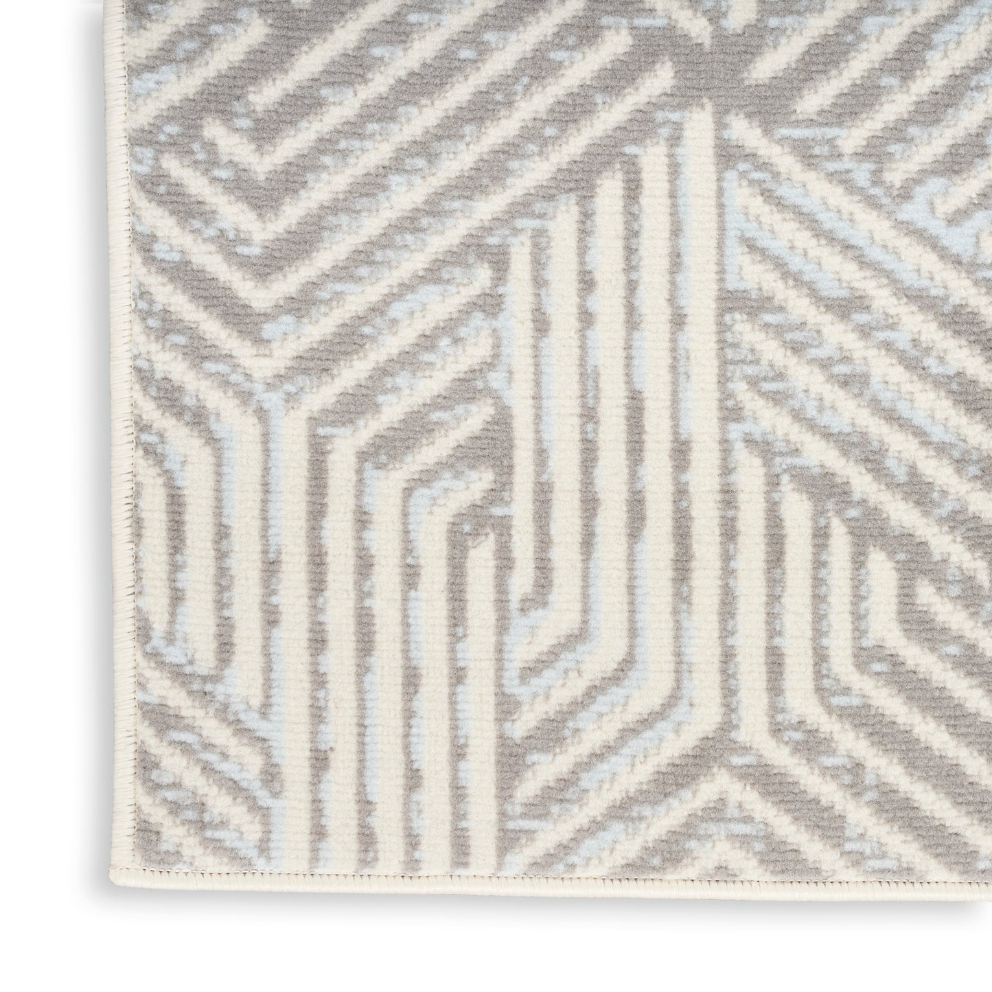 Close-up of a woven rug featuring a beige and white geometric maze pattern with a light cream border.