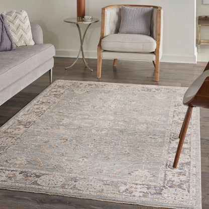 Living room rug in gray-beige pattern, light gray sofa, wood-framed armchair, throw pillows, dark wood floor.