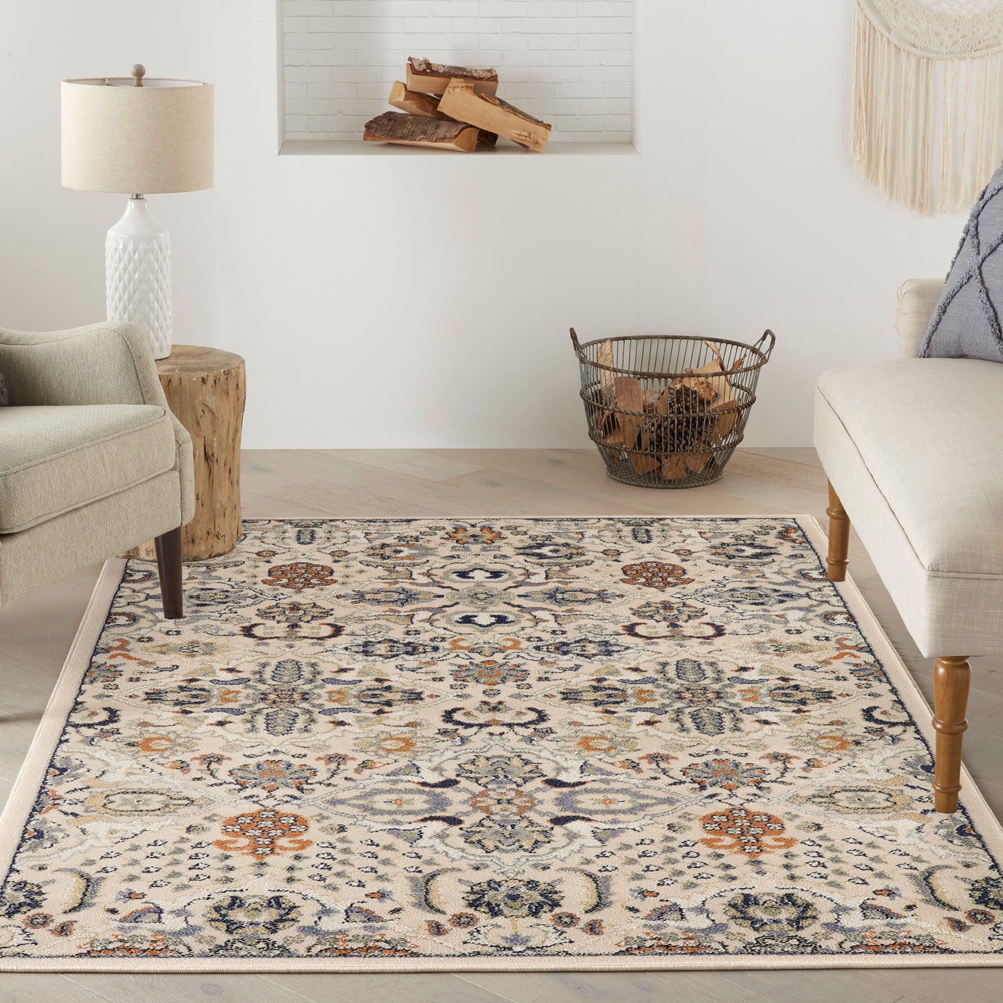 Neutral living room with ornate cream rug in blue/orange floral pattern, beige chairs, wood stump table, and firewood basket.