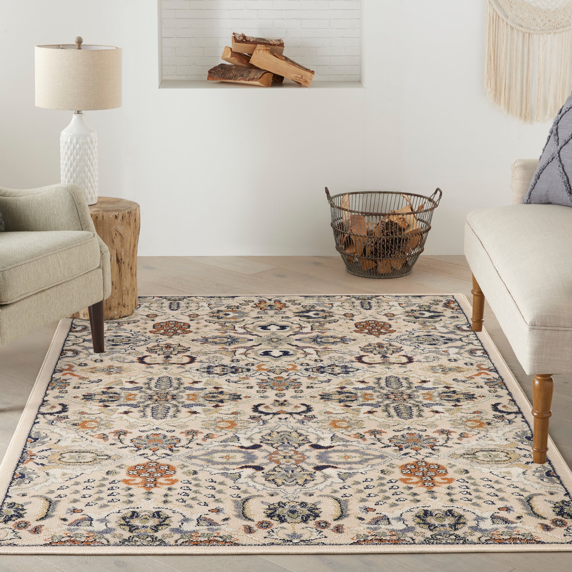Neutral living room with ornate cream rug in blue/orange floral pattern, beige chairs, wood stump table, and firewood basket.