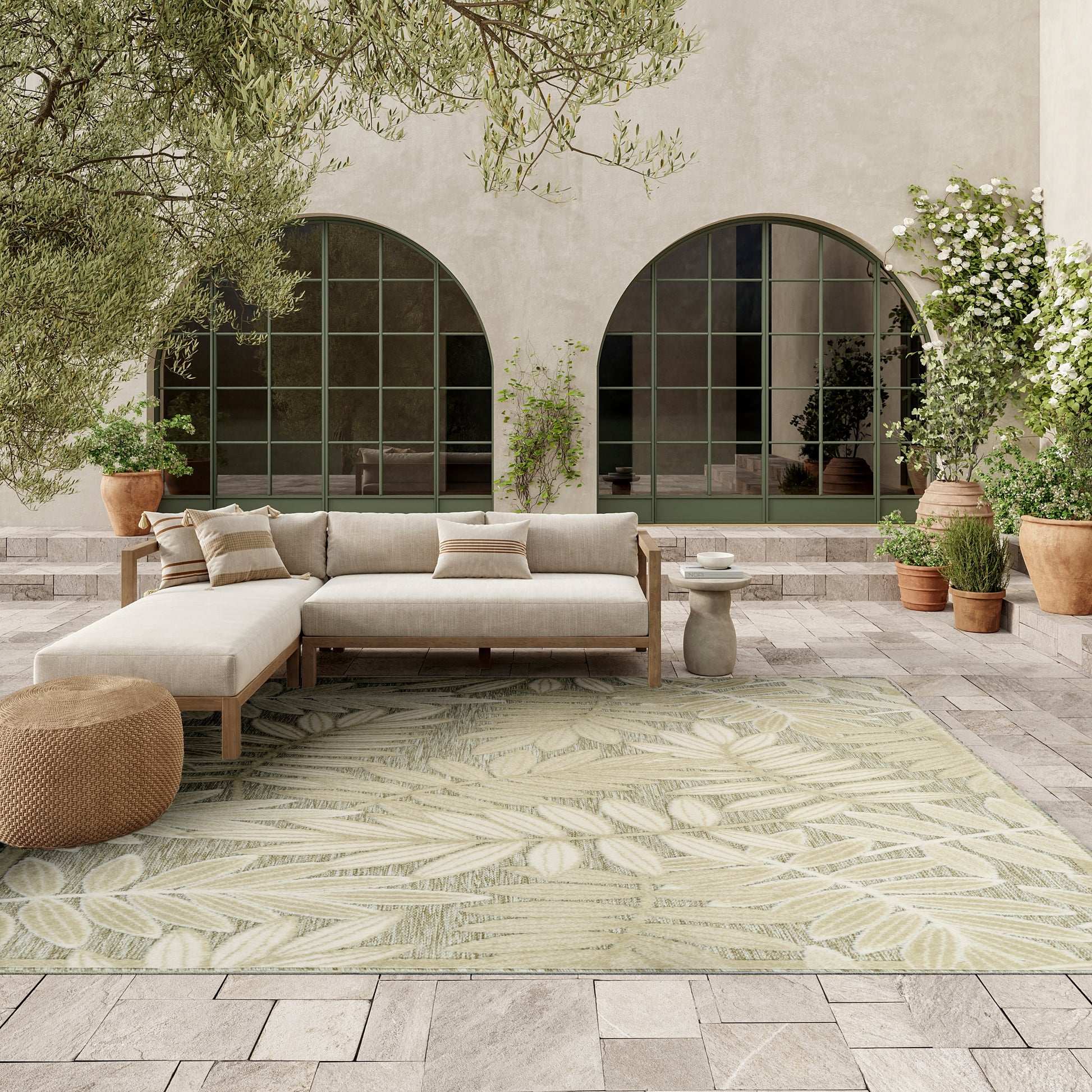 Palm-leaf rug on a wooden floor (8' x 11') with arched windows, potted plants, and a leafy courtyard setting.