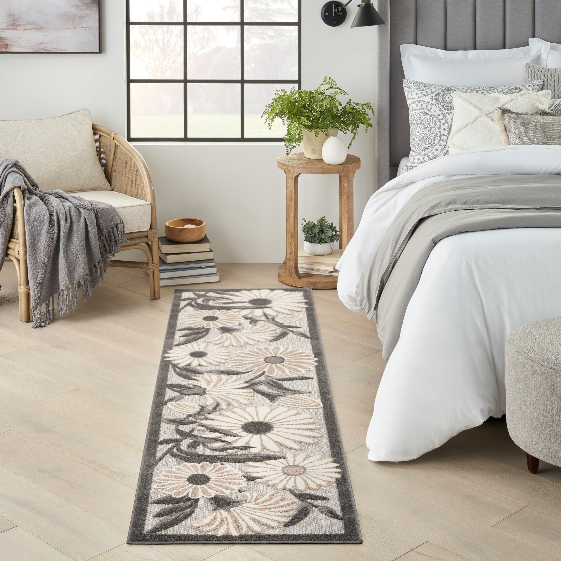 Long beige-gray floral runner rug on light wood floor beside a white bed and rattan chair.