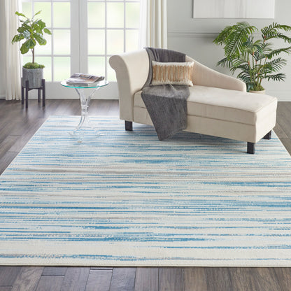 Beige chaise lounge on a blue striped area rug in a bright living room with plants and a glass side table.