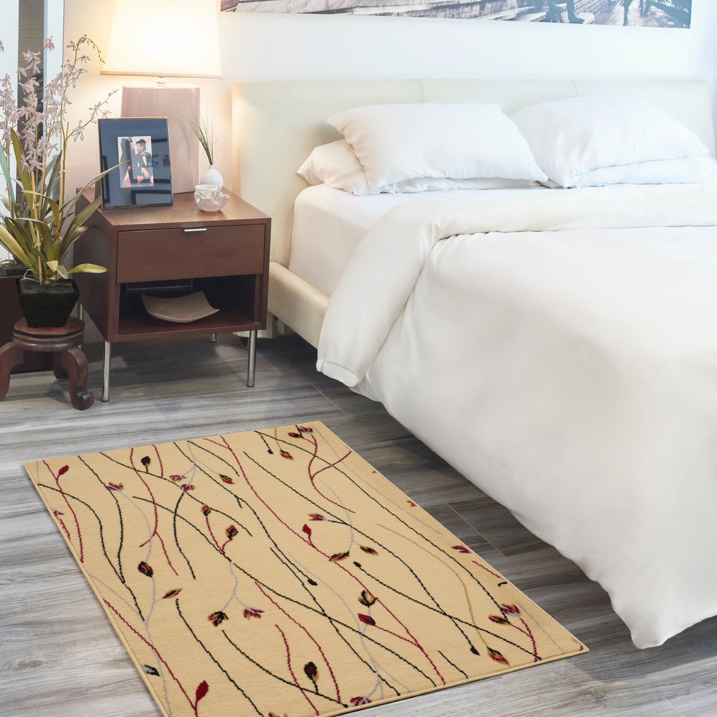 Beige area rug with multicolored wavy lines beside a white bed, dark wood nightstand, plant, and soft lamp light.