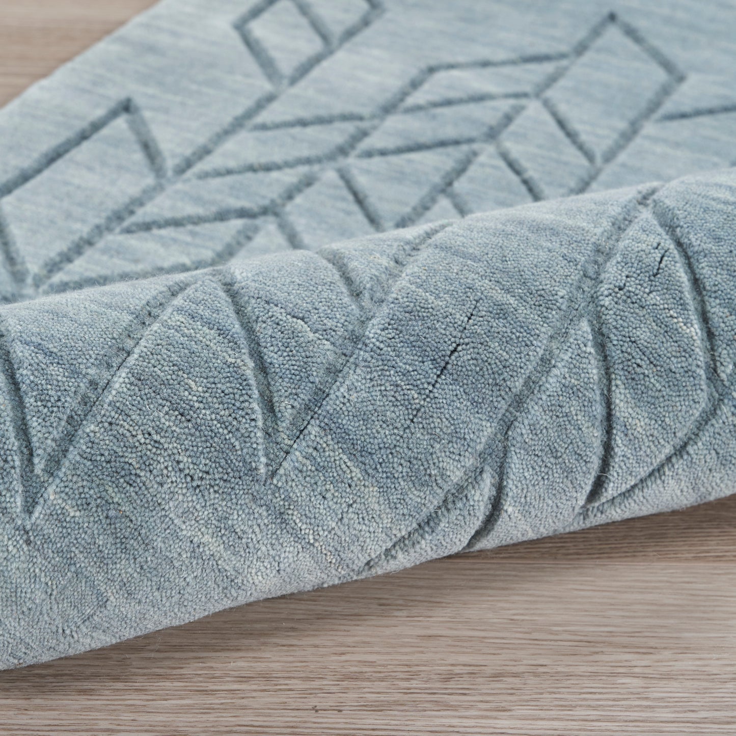 Blue rug with a geometric diamond pattern, plush textured pile, and a folded edge on a wooden floor.