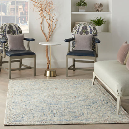 Living room with navy upholstered chairs, botanical backs, round marble-top table on brass base, pale sofa, and light rug.