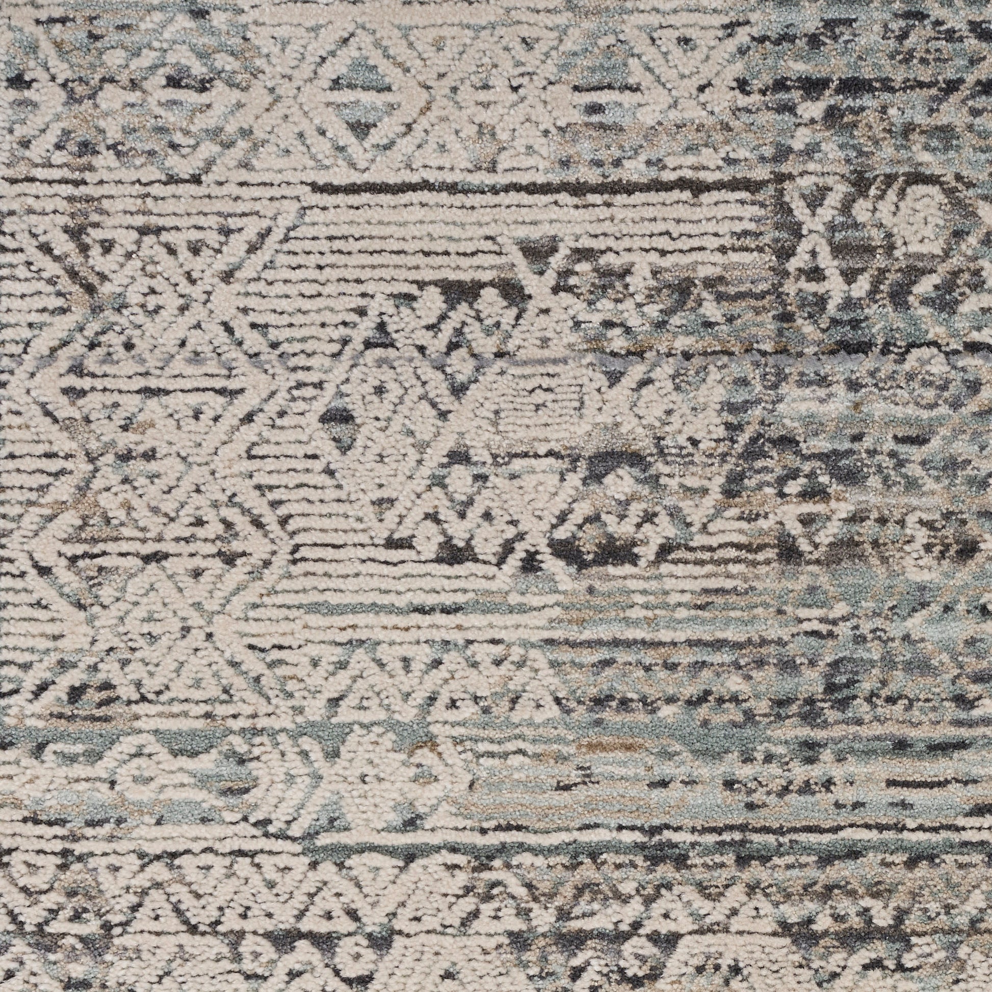 Distressed geometric rug with ivory and cream motifs on blue-gray background; tribal-inspired pattern and faded borders.