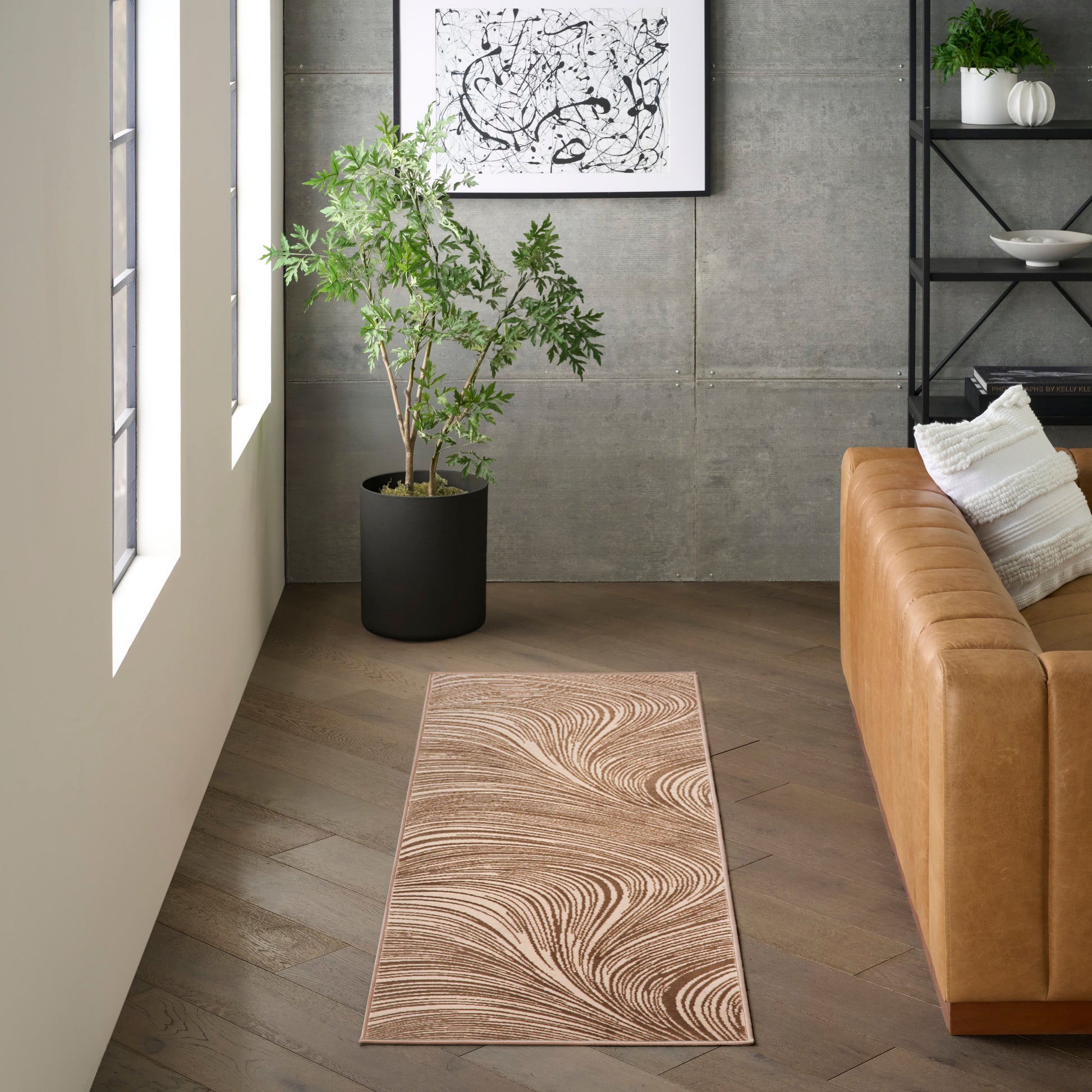 Beige swirl-pattern runner rug on wood floor beside a tan leather sofa in a contemporary living room with a plant.