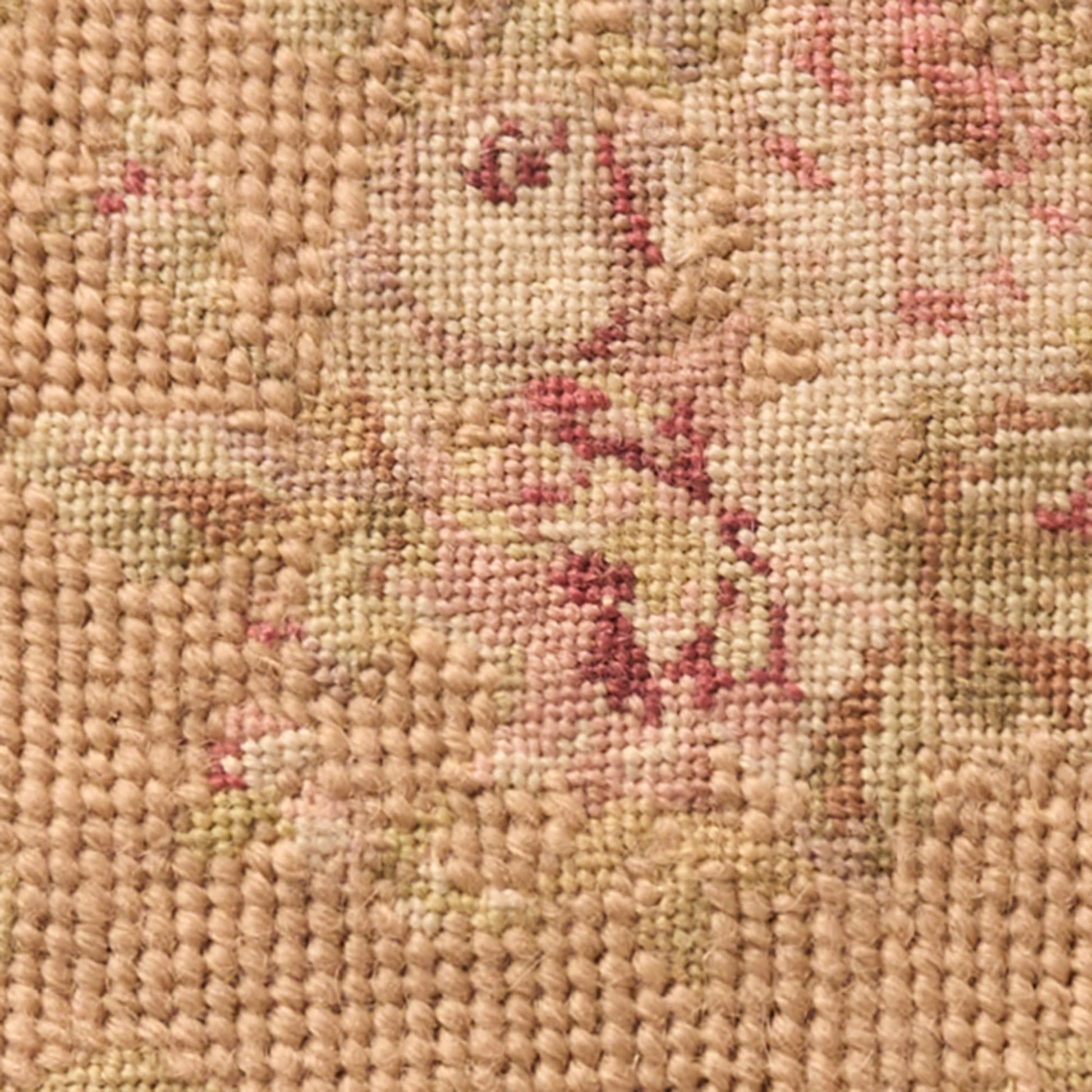 Close-up of a woven rug with beige background and pink floral motifs; textured, knotted fibers.