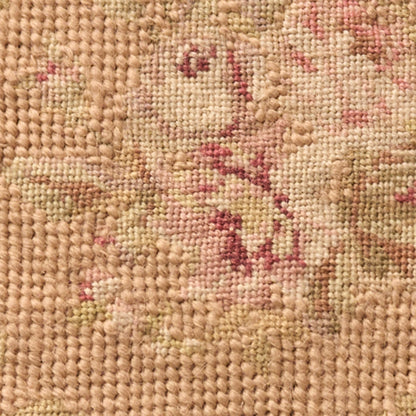Close-up of a woven rug with beige background and pink floral motifs; textured, knotted fibers.