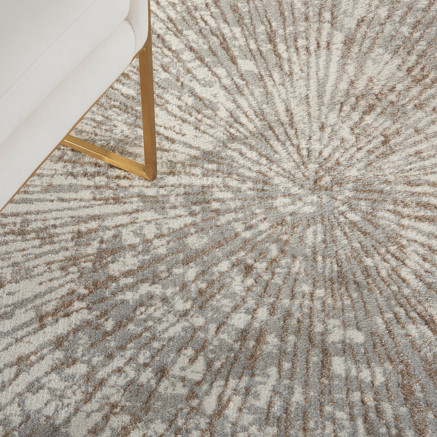 Beige area rug with brown sunburst radial pattern; 6' x 9' rug in a living room with a white sofa & gold metal legs.