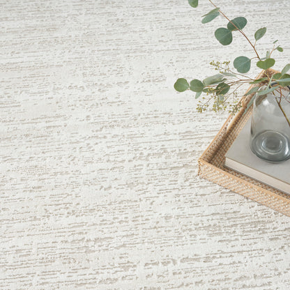Cream textured rug with a subtle pattern; wicker tray, glass vase with eucalyptus stems, and a book.