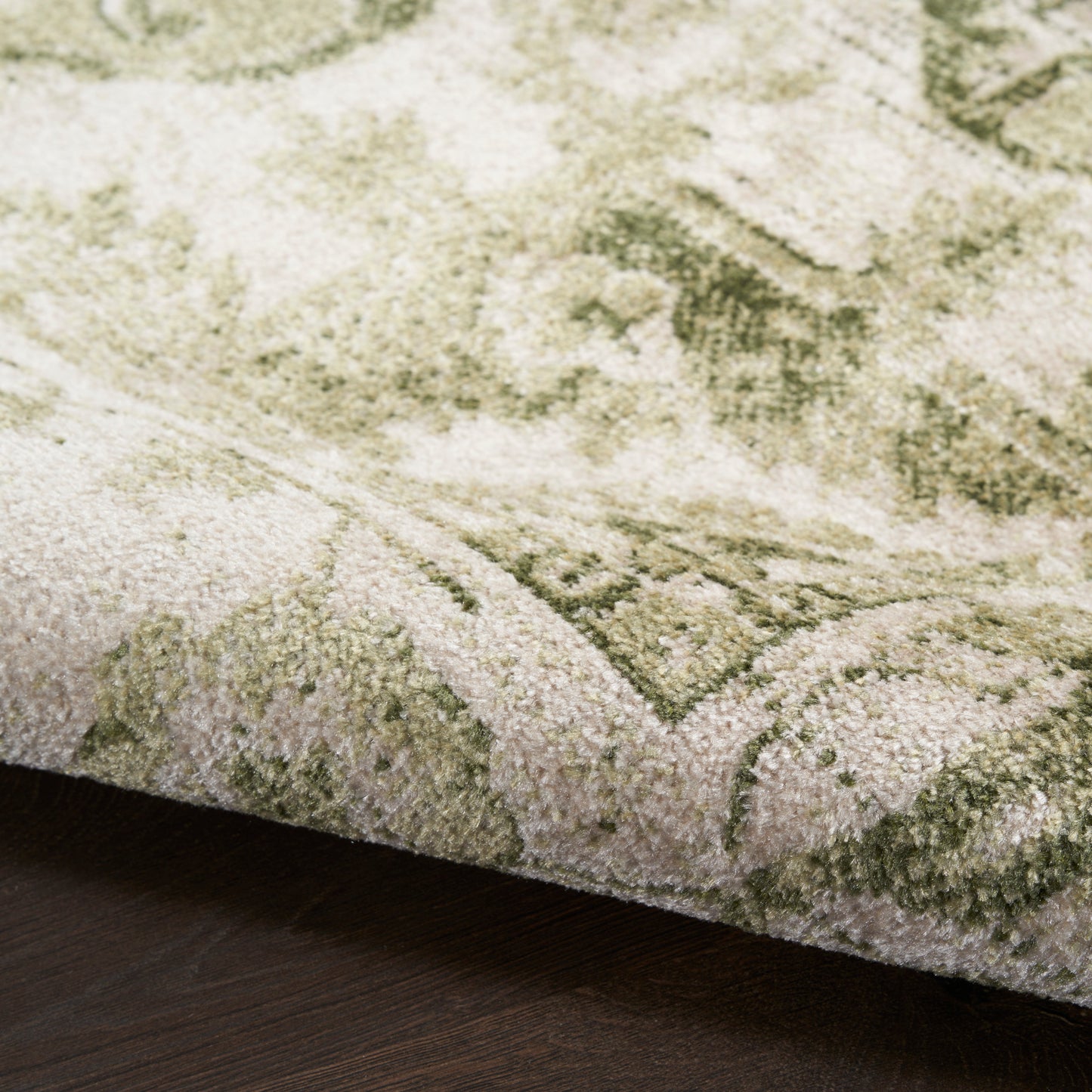 Close-up of a green and ivory patterned rug with a plush pile on dark wood flooring.
