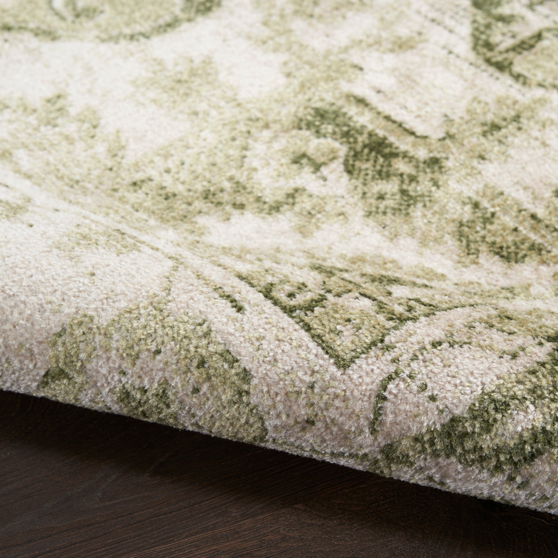 Close-up of a green and ivory patterned rug with a plush pile on dark wood flooring.
