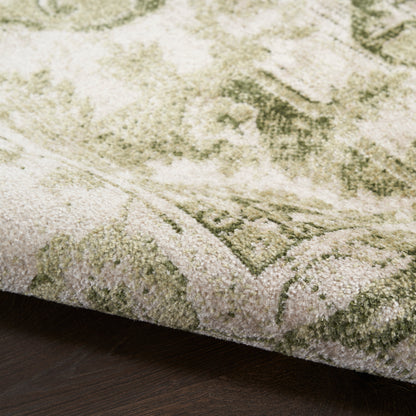 Close-up of a green and ivory patterned rug with a plush pile on dark wood flooring.