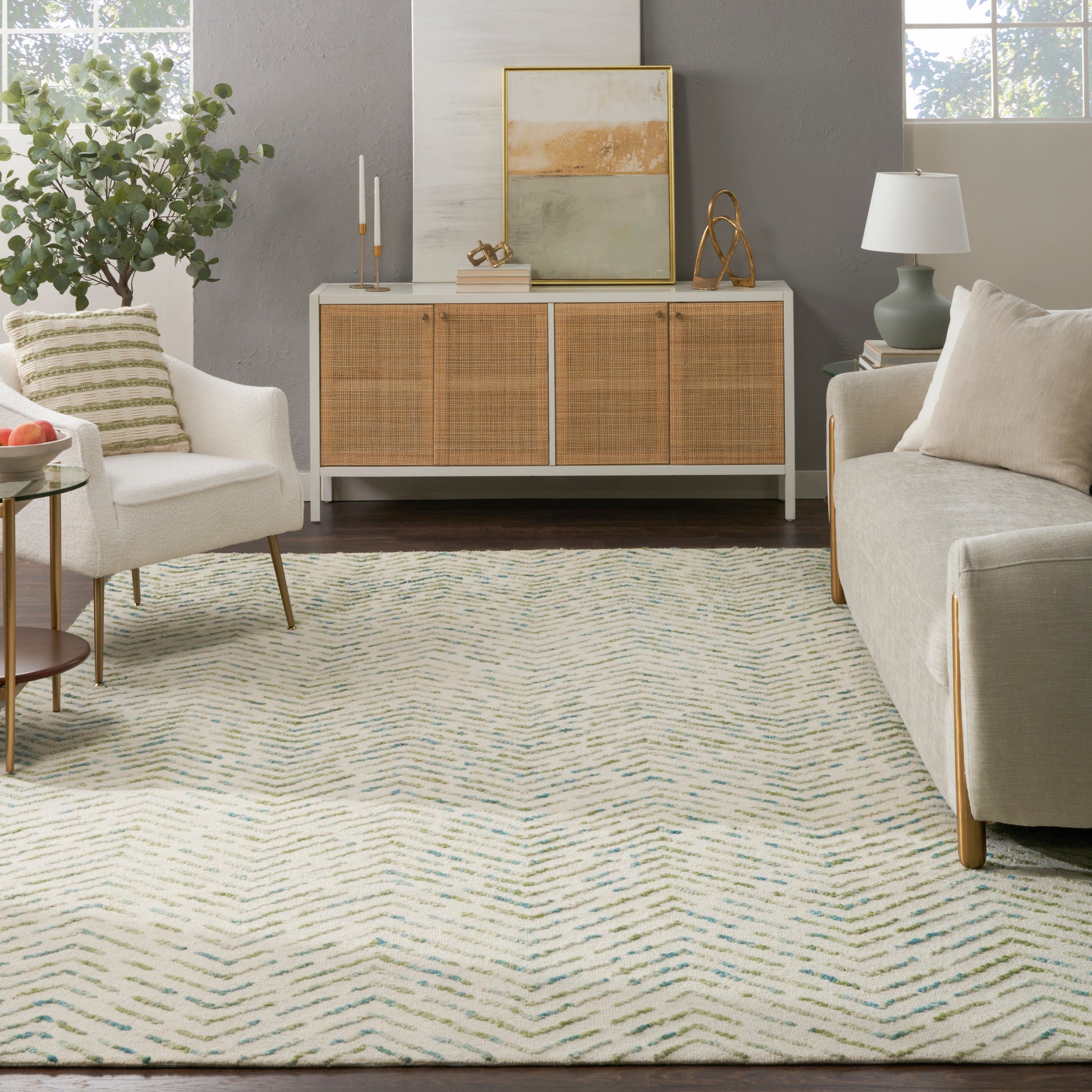 Cream sofa and armchair in a cozy living room with a woven rattan cabinet, abstract art, plant, and blue zigzag rug.