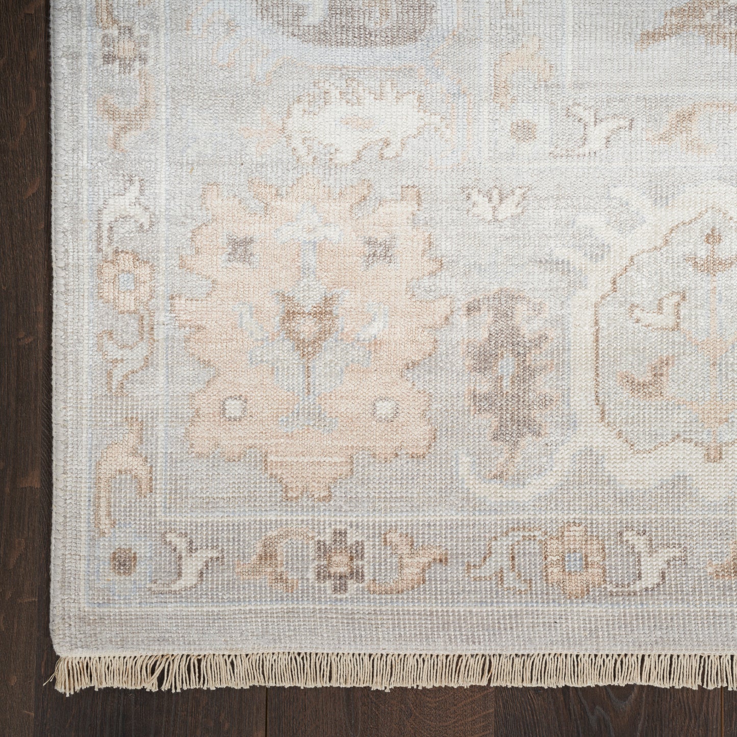 Cream and pale gray oriental rug with floral medallion pattern and fringe on dark wood floor.