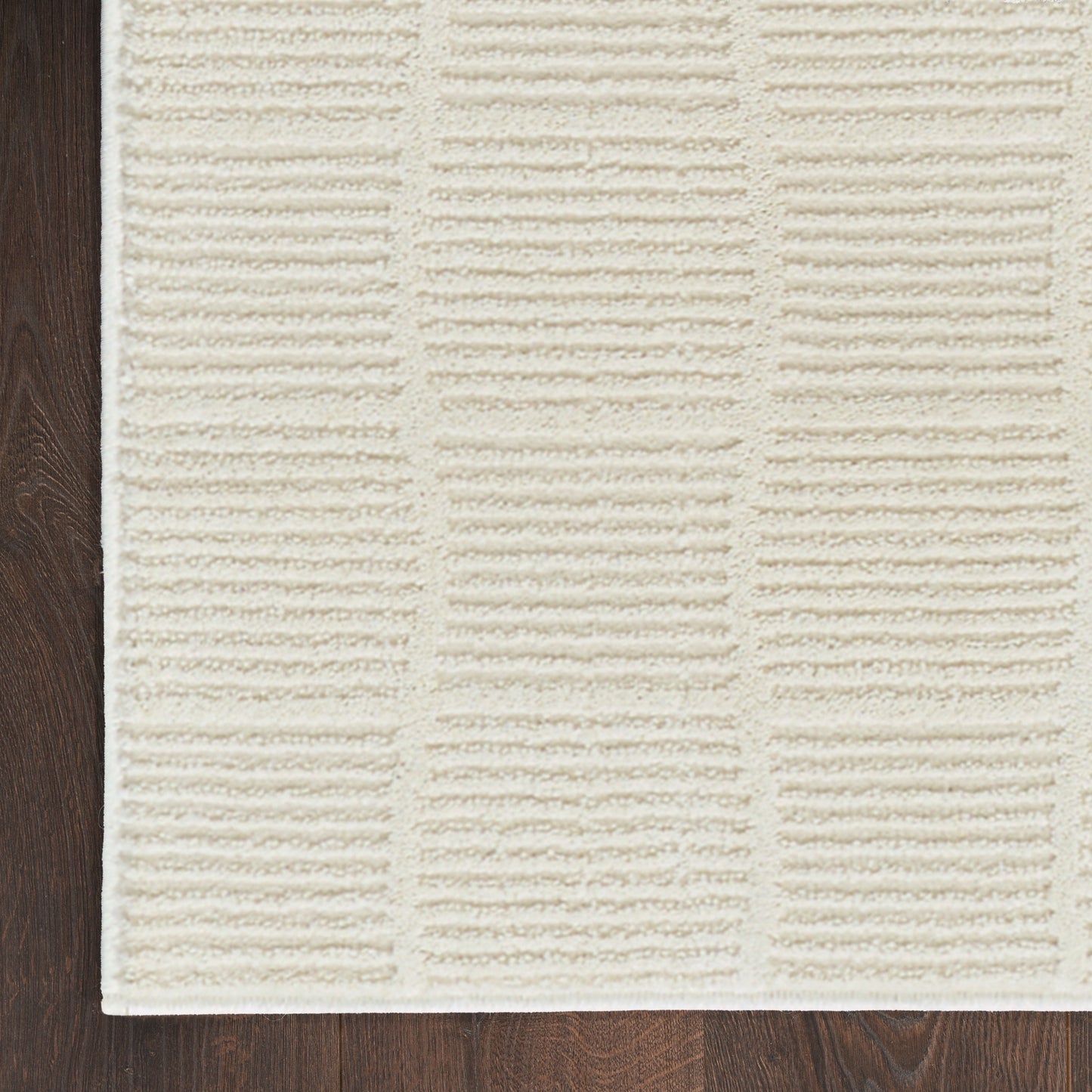 Cream textured rectangular rug with raised ribbed panel pattern on dark wood floor.