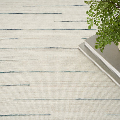 Cream textured rug with light blue horizontal stripes, gray book stack in corner, trailing green fern.