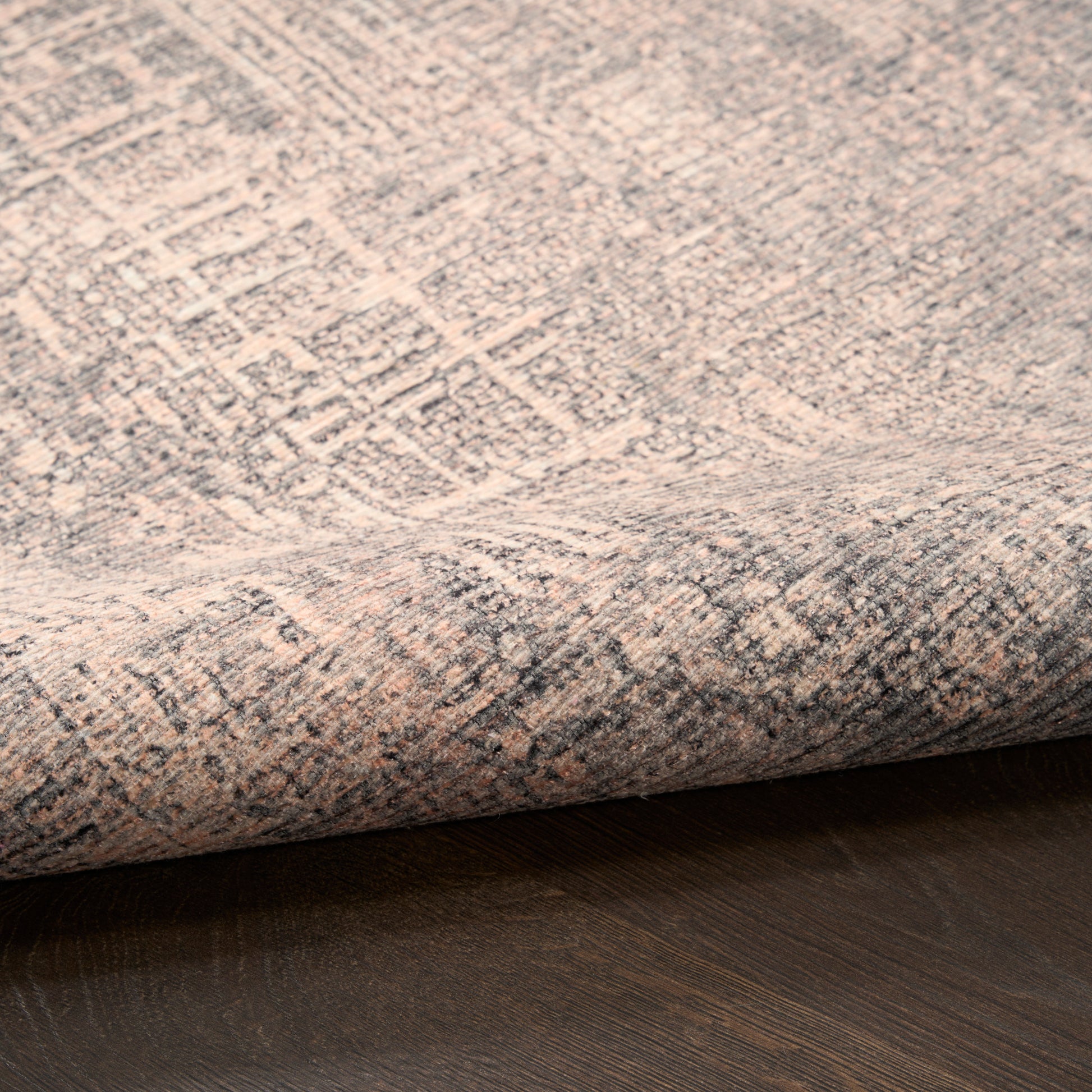 Beige and gray patterned rug with a rolled edge on a dark wood floor.