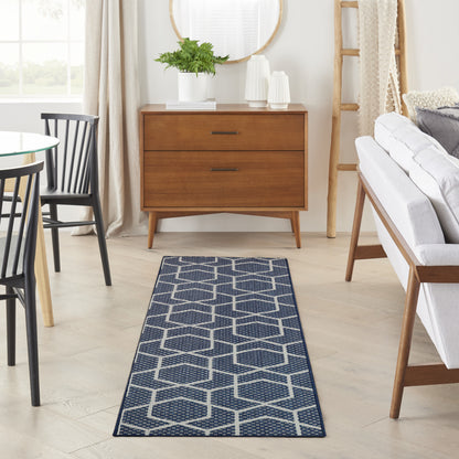 Wood mid-century dresser with two drawers, potted plant, round mirror; navy hexagon geometric runner rug in living room.