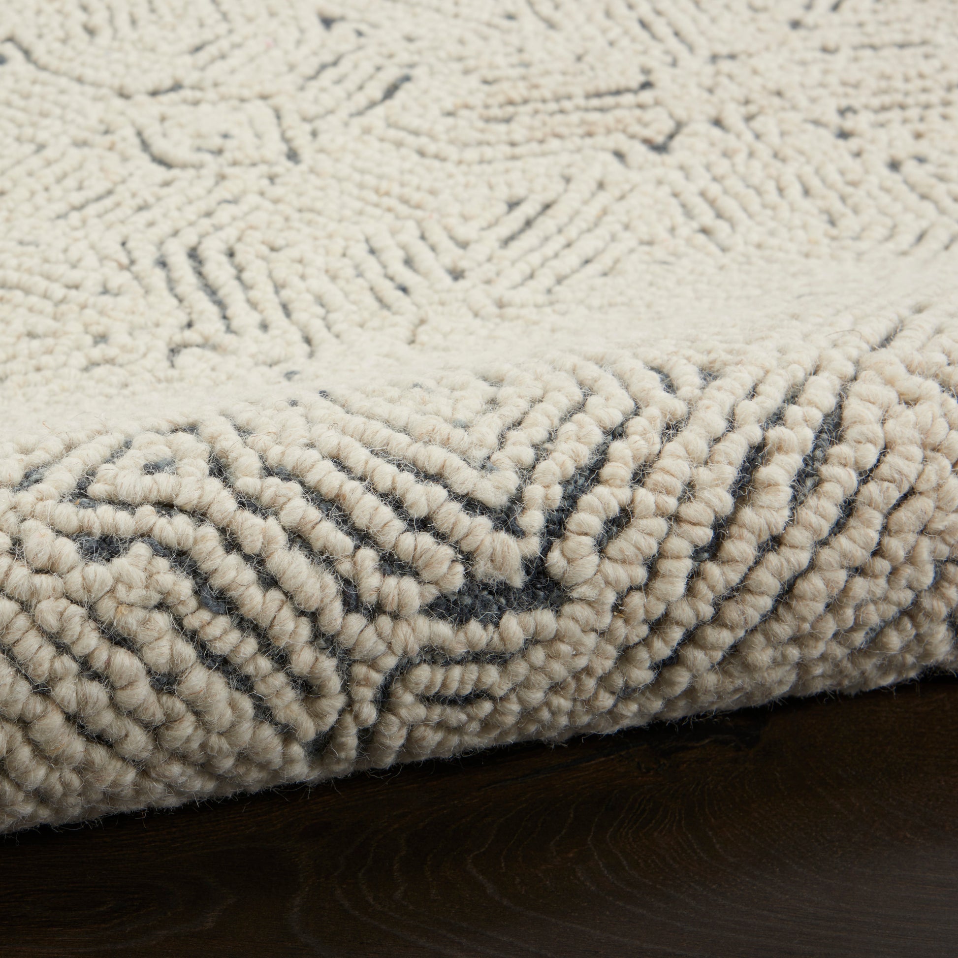 Cream looped-pile shag rug with subtle dark geometric edge pattern on dark wood floor.