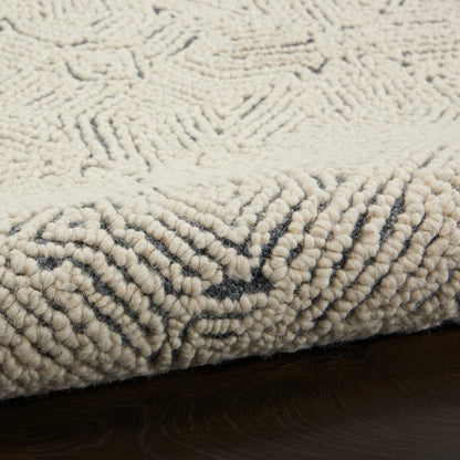 Cream looped-pile shag rug with subtle dark geometric edge pattern on dark wood floor.