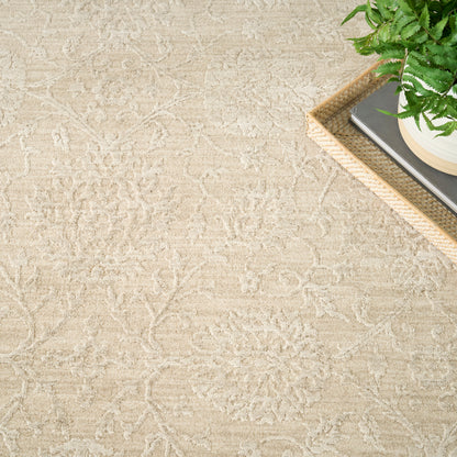 Beige patterned rug with floral motifs; corner view shows a woven tray with books & a potted fern.