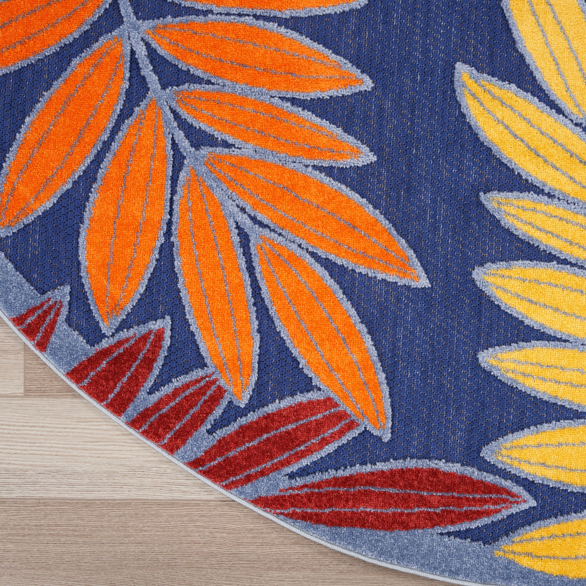 Round outdoor rug with orange, yellow and red leaf silhouettes on navy background; soft tufted textile.