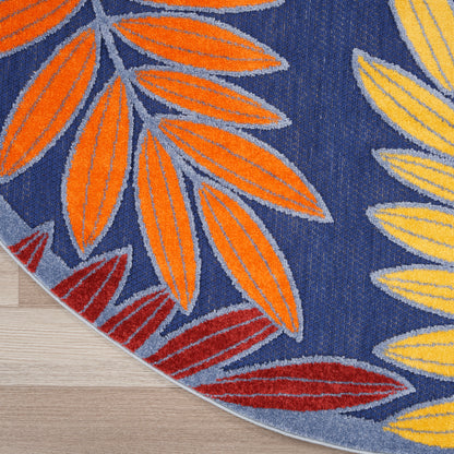 Round outdoor rug with orange, yellow and red leaf silhouettes on navy background; soft tufted textile.