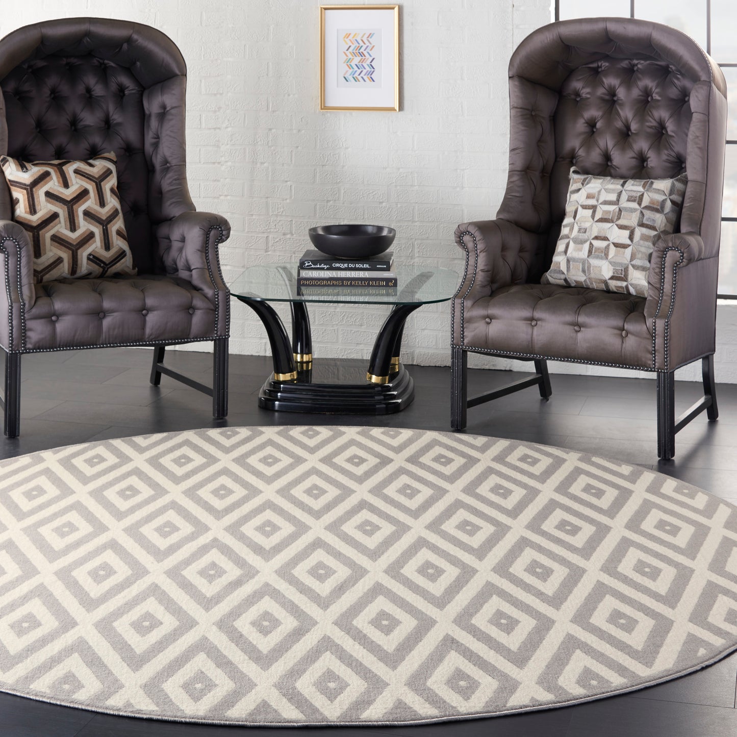 Beige geometric round rug under a seating area with two dark brown tufted leather wingback chairs featuring nailhead trim and a glass round coffee table.