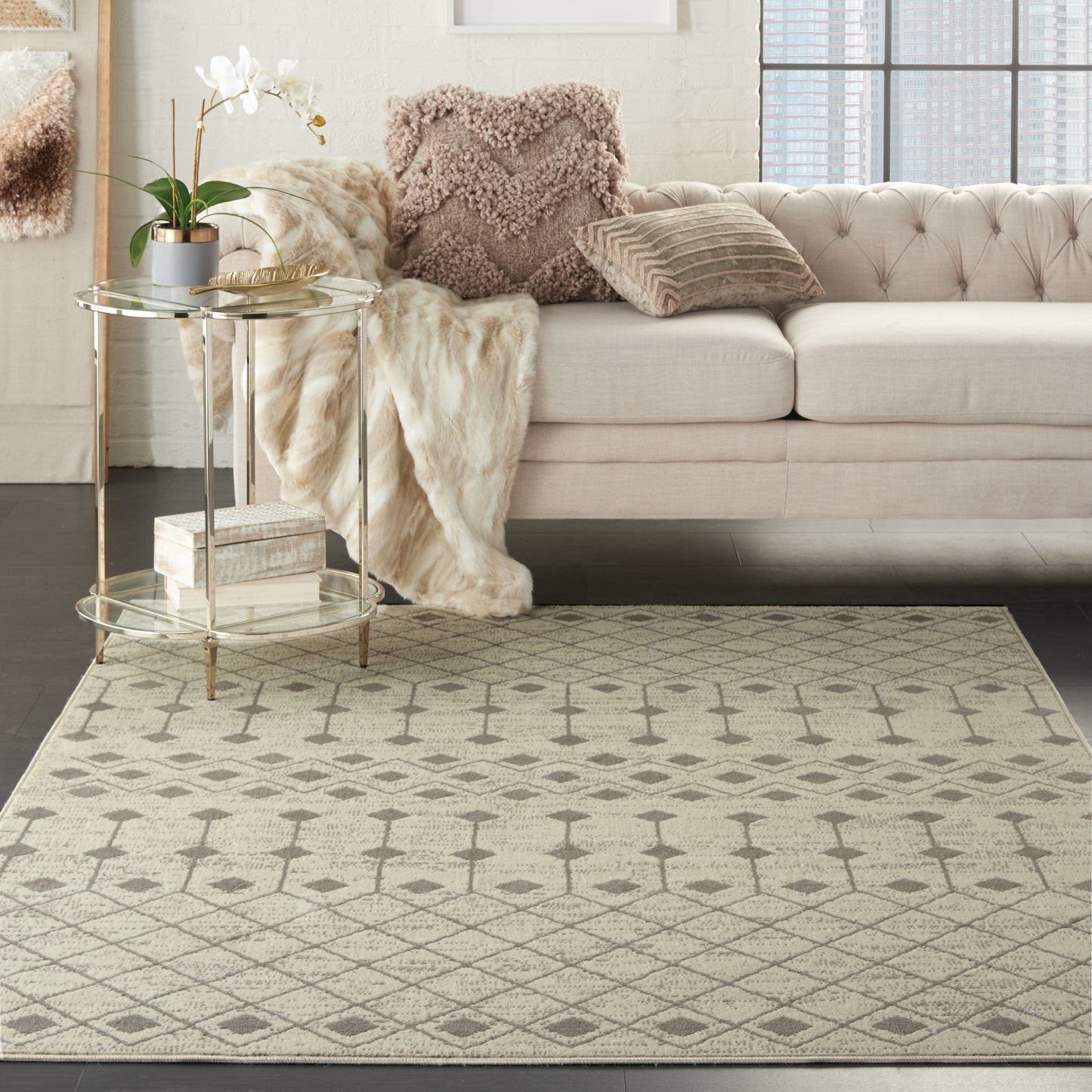 Geometric beige Bohemian area rug (5' x 7'), placed with a soft beige tufted sofa, plush pillows, fur throw, orchid, and a gold round side table.