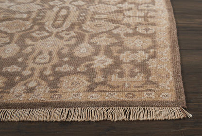 Beige and taupe patterned area rug with fringe edge on dark wood floor.