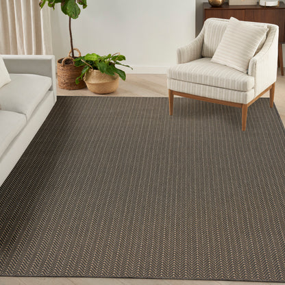 Dark brown herringbone woven rug in a modern living room with a light beige striped armchair on wood legs and potted plants.