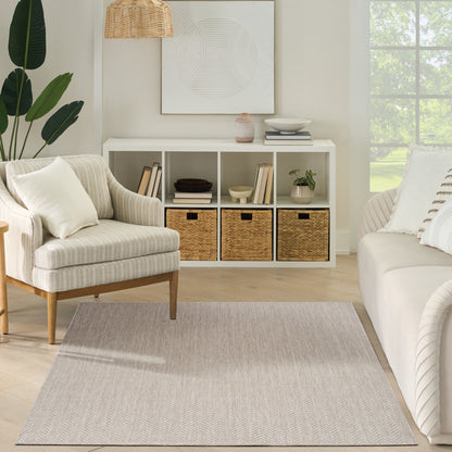 Neutral living room: beige upholstered armchair, white cubby unit with woven baskets, light chevron rug, greenery.