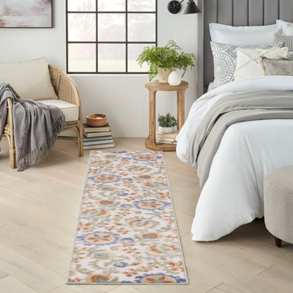 Long floral-pattern runner rug in beige with blue, orange and green accents on light wood floor in a cozy bedroom.