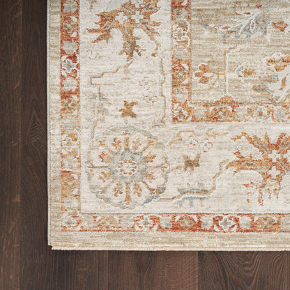 Beige vintage-style area rug with floral medallion border in coral, blue, and taupe on dark hardwood floor.