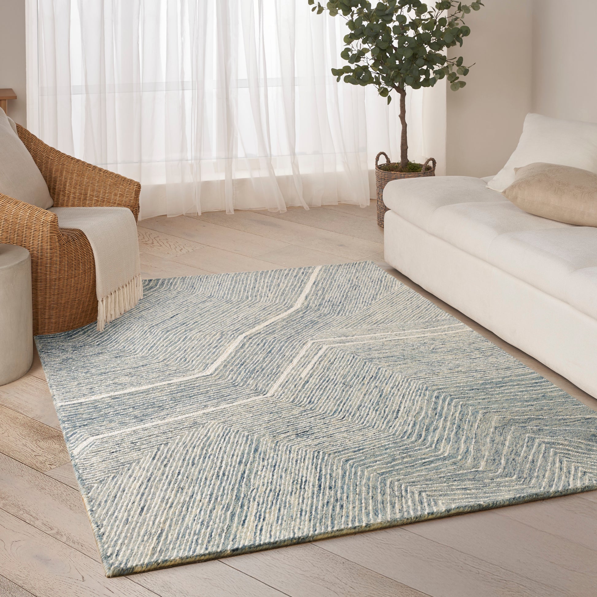 Rectangular pale blue-gray flatweave rug with chevron pattern in a bright modern living room.