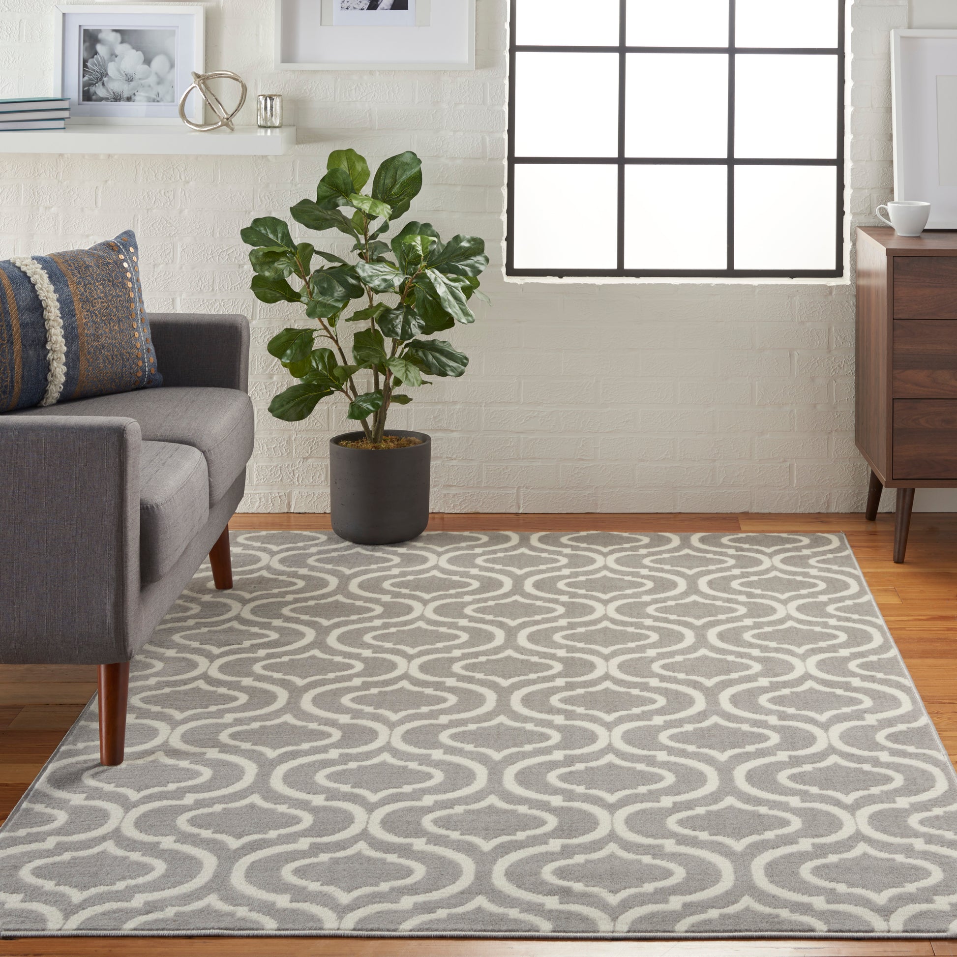 Gray area rug with white trellis pattern in a modern living room beside a gray sofa, green plant, and wooden dresser.