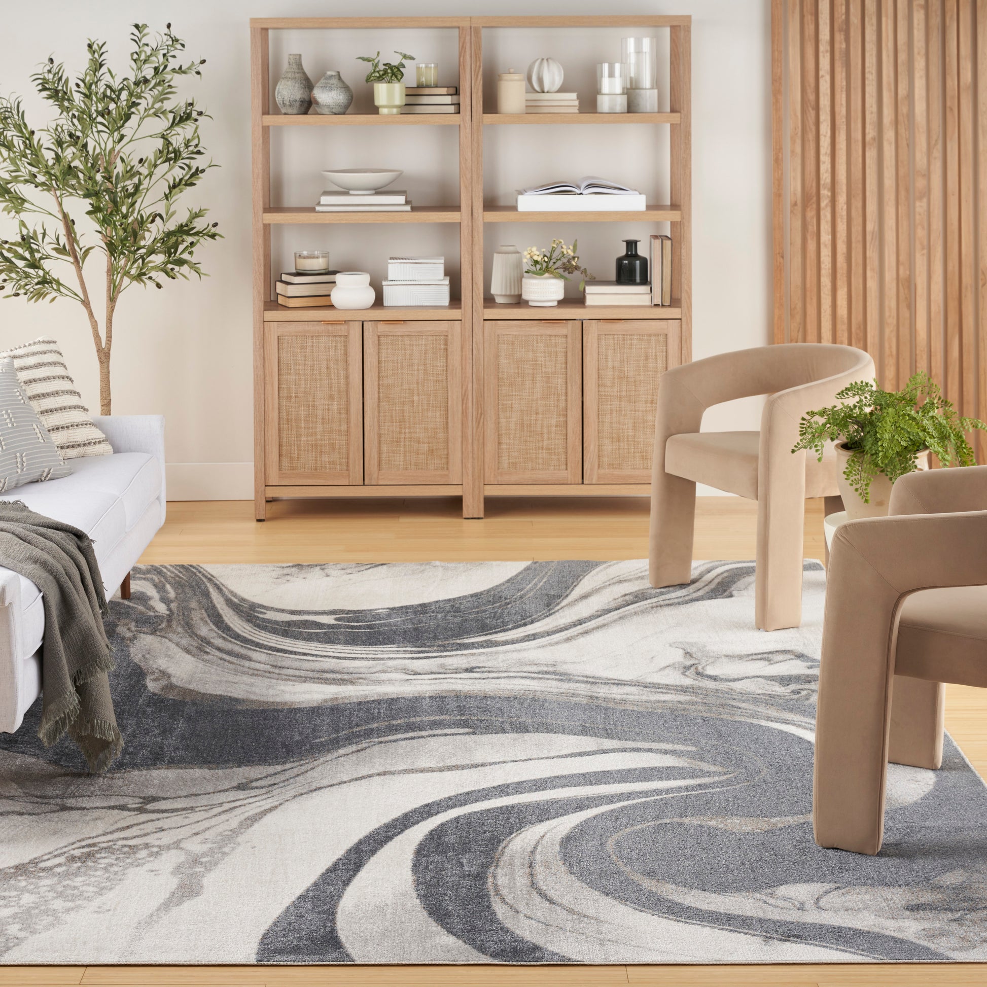 Light wood bookcase with open shelves, beige curved lounge chairs, and a gray-blue abstract rug in a modern living room.